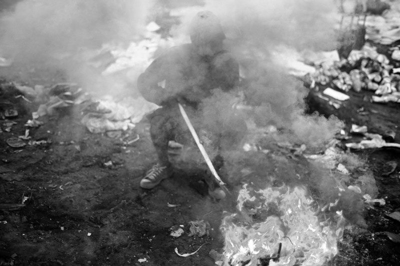 A young boy covered by smoke while burning small pieces of electronics. The electronics arrive at the dumpsite in which he lives via the refuse system in Maputo, which does not process or recycle any rubbish thrown out by previous owners.